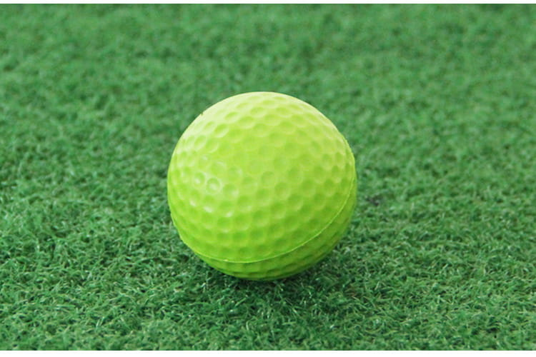 Lightweight foam golf ball in bright neon green on artificial turf